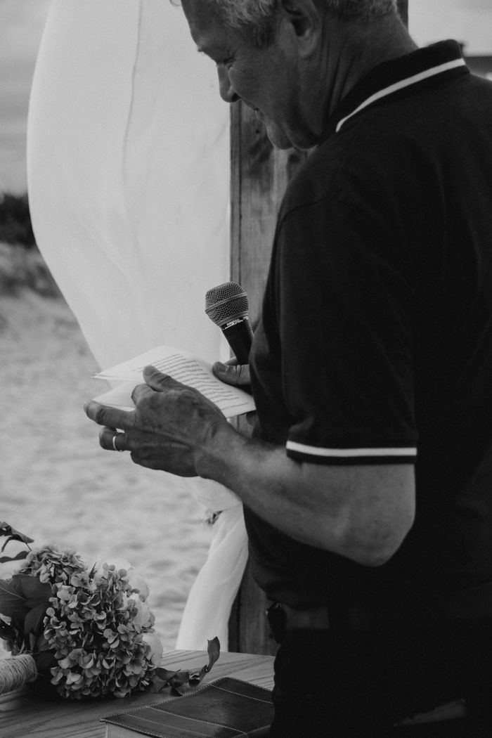 services-02 Monochromatic photo of an elderly man giving a speech at a beachside event.