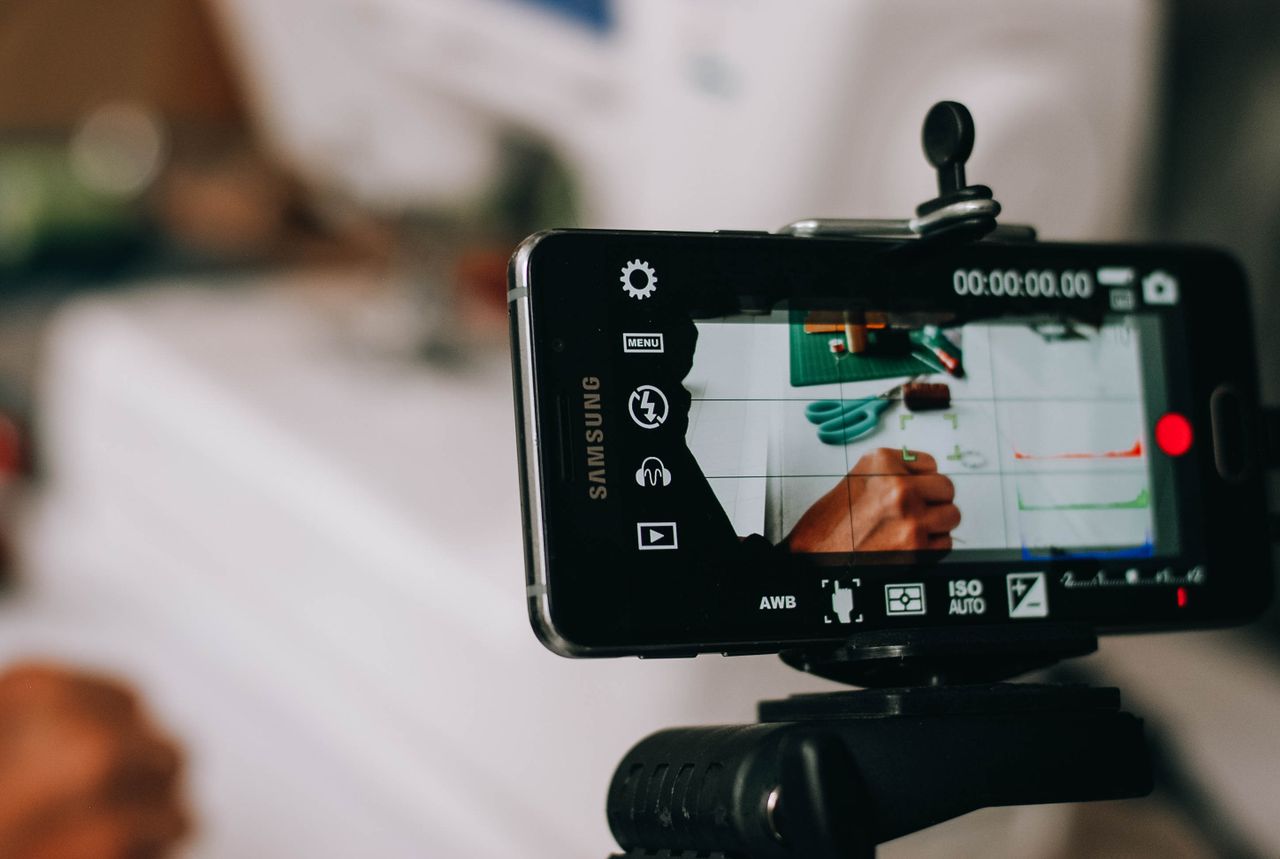 who-are-we-02 Smartphone on tripod capturing person writing on paper, showing content creation process.